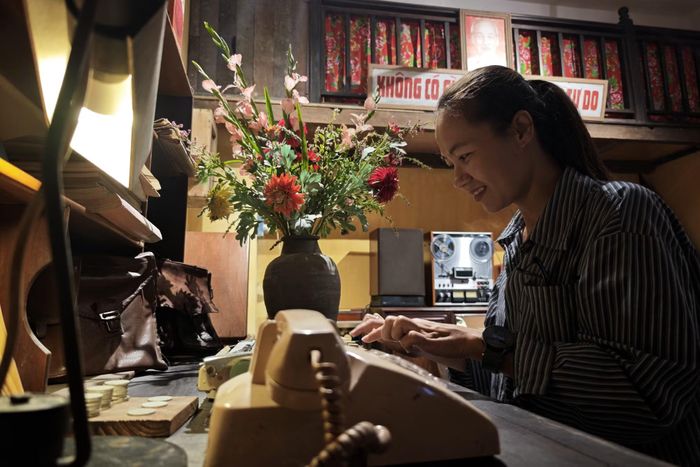 Chị Phạm Thị Việt Hồng trải nghiệm gõ máy chữ cơ bên bàn làm việc và bình hoa thược dược ngày Tết.