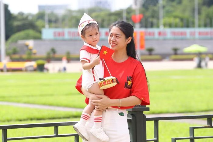 Trong vòng tay mẹ, em nhỏ khoác lên mình trang phục Đội Thiếu niên Tiền phong Hồ Chí Minh, lưu giữ khoảnh khắc đáng nhớ bên Lăng Bác