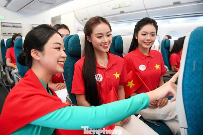 Hai thí sinh Hoa hậu Việt Nam 2026 được tiếp viên hướng dẫn cách sử dụng màn hình giải trí trên chuyến bay. Thí sinh Nguyễn Thục Uyên Nhi (ngoài cùng bên phải) cho biết cô trào dâng cảm xúc tự hào trên chuyến bay đặc biệt.