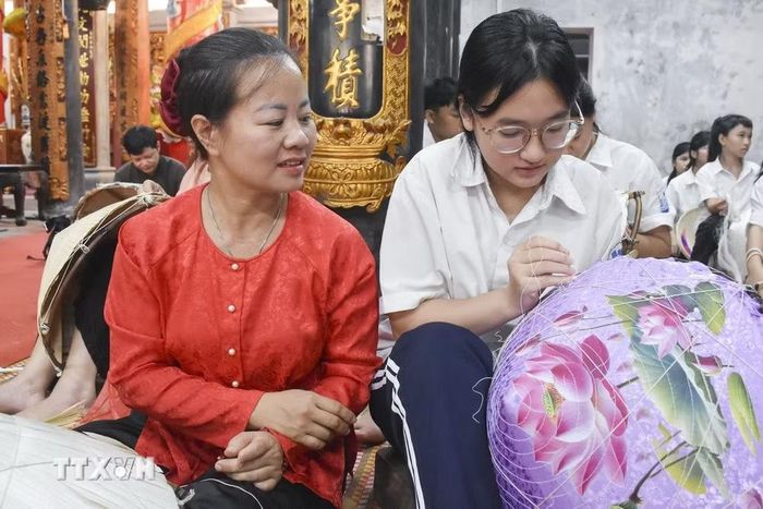 Nghệ nhân làm nón lá truyền thống làng Chuông truyền nghề cho thế hệ trẻ. (Ảnh: Nguyễn Cúc/TTXVN)