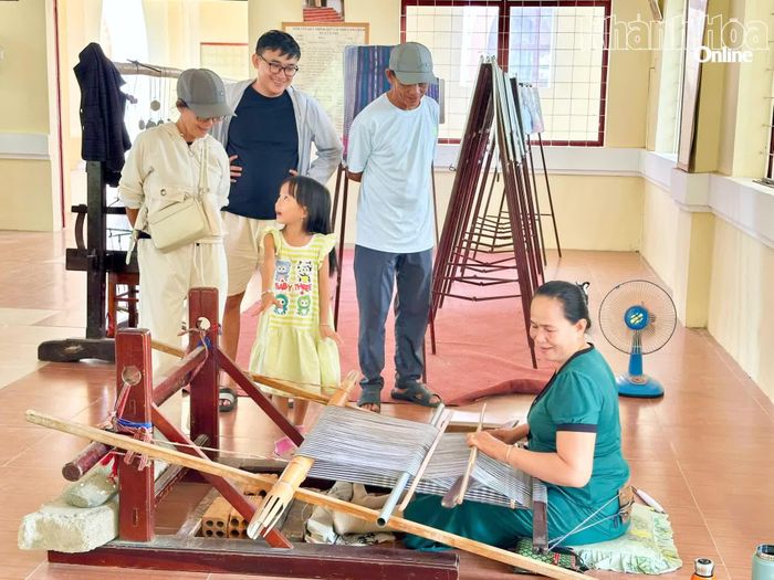 Một gia đình đến từ Cam Ranh thích thú xem nghệ nhân trình diễn dệt thổ cẩm truyền thống tại làng Mỹ Nghiệp.