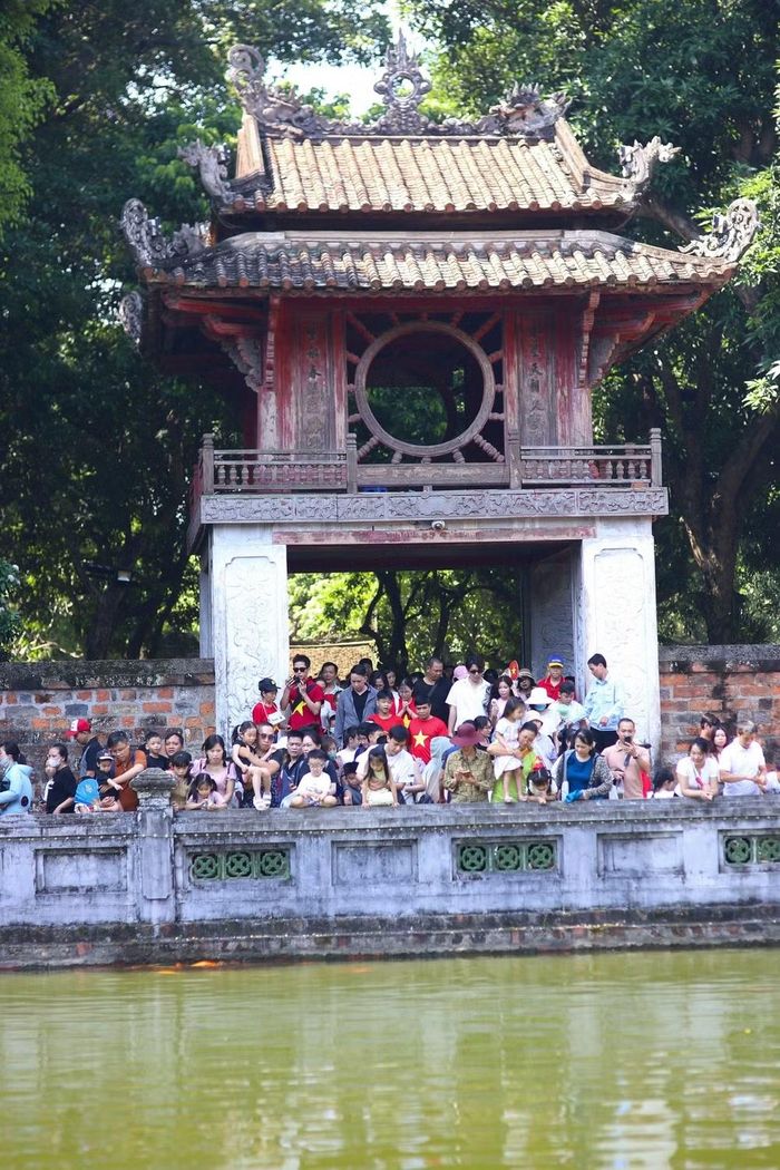 Nhiều du khách đứng trước Khuê Văn Các, theo dõi những đàn cá vàng nổi lên mặt nước