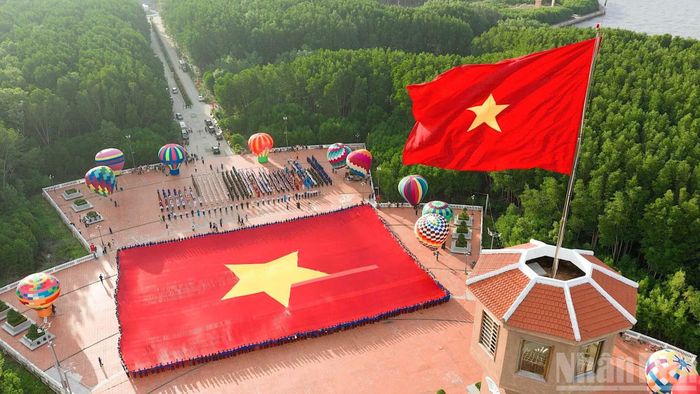 Lá cờ Tổ quốc kiêu hãnh tung bay trên đỉnh Cột cờ Hà Nội tại Đất Mũi, phía dưới là đại kỳ kỷ lục được hàng trăm đoàn viên, thanh niên Cà Mau giữ vững. (Ảnh: HỮU TÙNG)