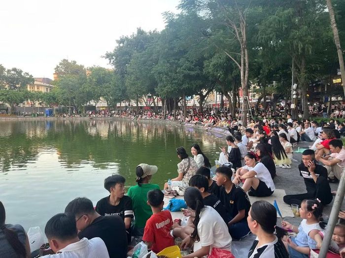 Khoảng 17h chiều không khí quanh khu vực Hồ Gươm bắt đầu nhộn nhịp khi các gia đình và nhóm bạn trẻ chủ động tới sớm để chọn vị trí quan sát thuận lợi nhất. Nhiều người dân cẩn thận chuẩn bị quạt mát vật dụng cá nhân và tranh thủ nghỉ ngơi trong lúc kiên nhẫn chờ đợi nhiều giờ trước thời điểm pháo hoa khai màn.