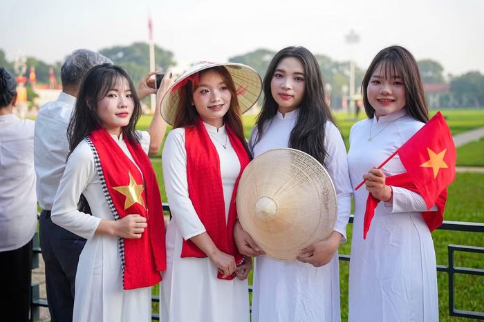 Các cô gái mặc áo dài trắng, cầm cờ Tổ quốc, đội nón lá hoặc quàng khăn rằn, tạo nên những hình ảnh nổi bật giữa dòng người.