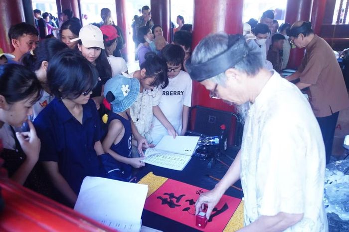 Du khách trải nghiệm xin chữ thư pháp tại Văn Miếu - Quốc Tử Giám. Mỗi tờ giấy điệp xin chữ có giá 200.000 đồng, thu hút nhiều gia đình, đặc biệt là các em nhỏ. Văn Miếu - Quốc Tử Giám là một trong những địa chỉ hàng đầu để các gia đình xin chữ, dạy trẻ về đạo học.