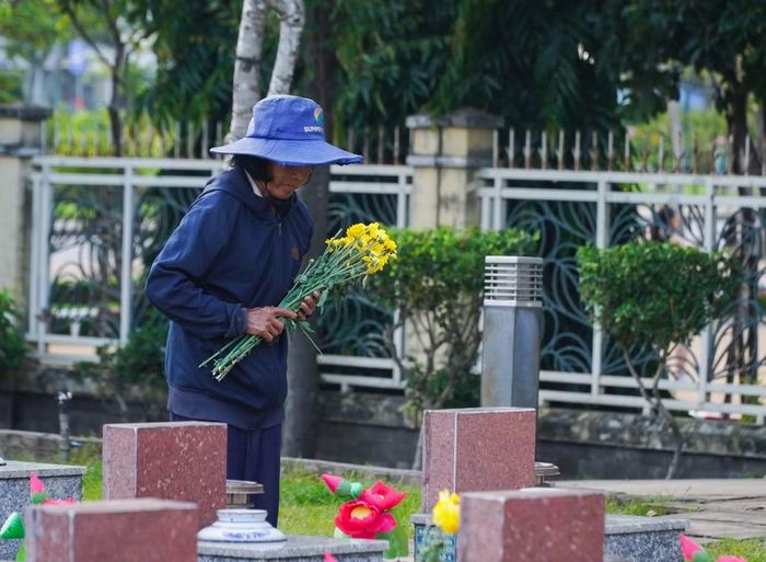Bà Hiệp thu dọn hoa đã héo, lau chùi lại các bia mộ.
