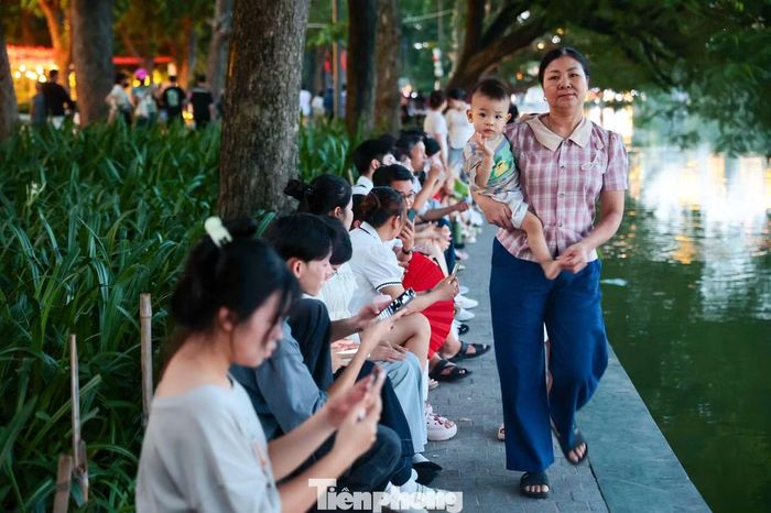 Càng về tối, những khoảng trống quanh Hồ Gươm dần được lấp kín. Nhiều người chấp nhận ngồi chờ hàng giờ để giữ vị trí đẹp.