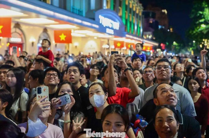 Nhiều người giơ cao điện thoại, máy ảnh ghi lại khoảnh khắc pháo hoa phủ kín bầu trời trung tâm Thủ đô.