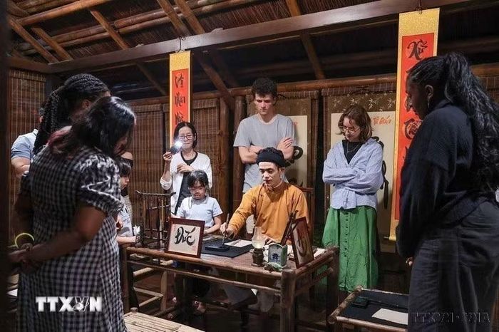 Văn hóa được bảo tồn và phát huy. Trong ảnh: Du khách theo dõi nghệ nhân trình diễn thư pháp trong không gian văn hóa truyền thống tại tour đêm Văn Miếu. (Ảnh: Phạm Tuấn Anh/TTXVN) ​ ​
