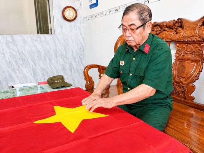 Cựu chiến binh Lê Minh Điểu nâng niu lá cờ Tổ quốc, biểu tượng thiêng liêng gắn với một đời chiến đấu và ký ức không quên của ông