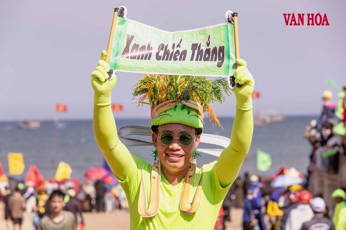 Một cổ động viên đội bó lúa chín, mặc trang phục xanh và giơ cao tấm bảng “Xanh chiến thắng”. Cách hóa trang vui nhộn, sáng tạo góp thêm sắc màu trẻ trung cho lễ hội truyền thống của làng biển
