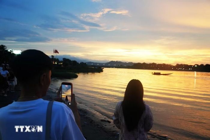 Giới trẻ chụp ảnh lưu lại cảnh đẹp của hoàng hôn từ bờ Nam sông Hương, thành phố Huế. (Ảnh: Nguyên Lý/TTXVN)