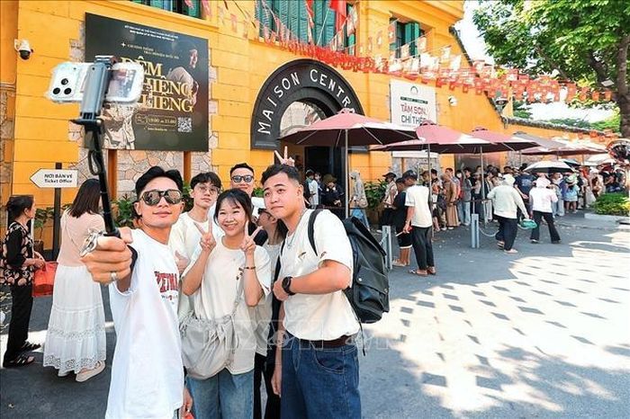 Nhiều bạn trẻ tranh thủ ghi lại khoảnh khắc bên Di tích Nhà tù Hỏa Lò trong khi phía sau, dòng khách vẫn nối dài chờ vào tham quan. Ảnh: Phạm Tuấn Anh/TTXVN