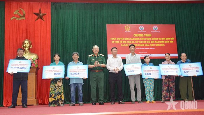 Trung tướng, Anh hùng LLVT nhân dân Nguyễn Đức Soát, nguyên Phó tổng Tham mưu trưởng, Chủ tịch Hội Hỗ trợ khắc phục hậu quả bom mìn Việt Nam và ông Huỳnh Văn Tịnh, Phó bí thư Thường trực Đảng ủy xã Sơn Tịnh trao hỗ trợ sinh kế cho nạn nhân bom mìn. Bà Phan Thị Nguyệt đứng ở ngoài cùng bên phải. Ảnh: NGỌC MINH