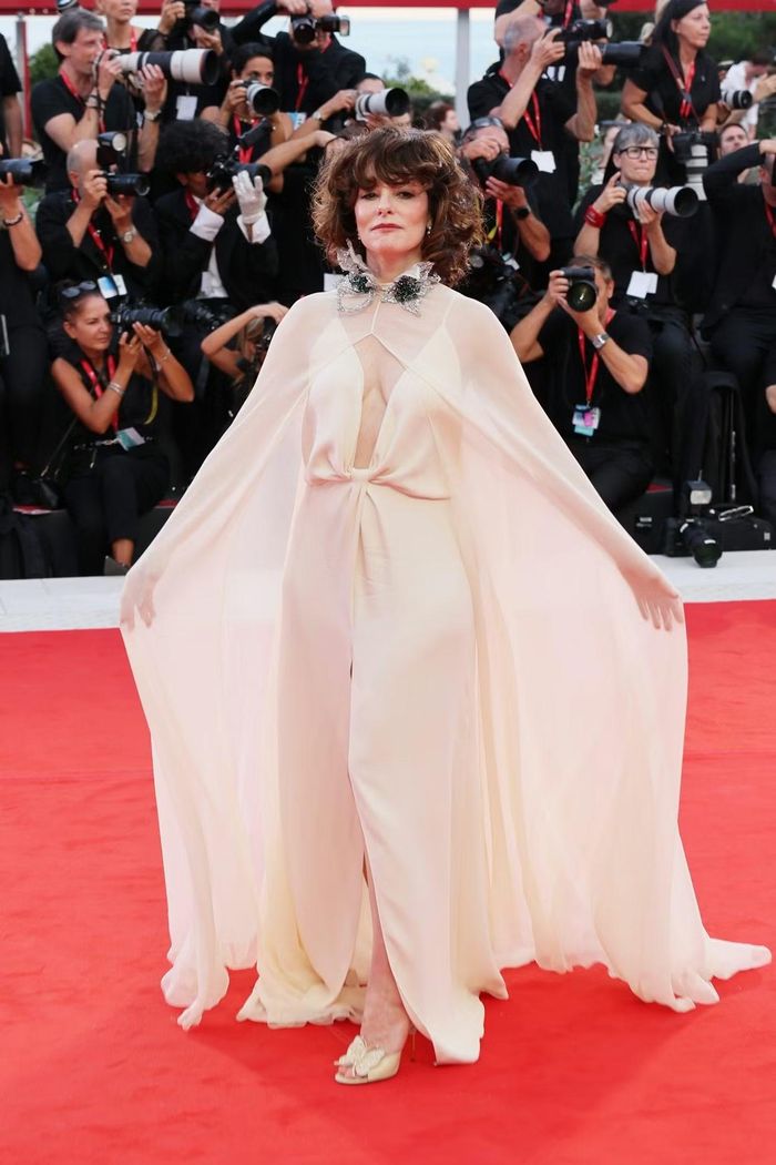 Parker Posey tạo dáng trong thiết kế Valentino của Alessandro Michele. Mẫu váy màu kem được xử lý theo cấu trúc áo choàng, sử dụng nhiều lớp vải mềm và phom rộng. Nữ diễn viên hoàn thiện diện mạo bằng bộ trang sức đá màu xanh.