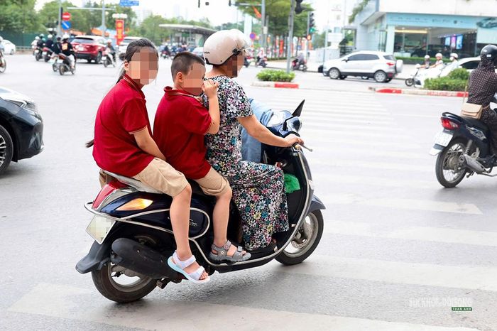 Một phụ huynh chở hai trẻ trên xe máy, cả hai trẻ đều không đội mũ bảo hiểm. Ảnh: T.Anh