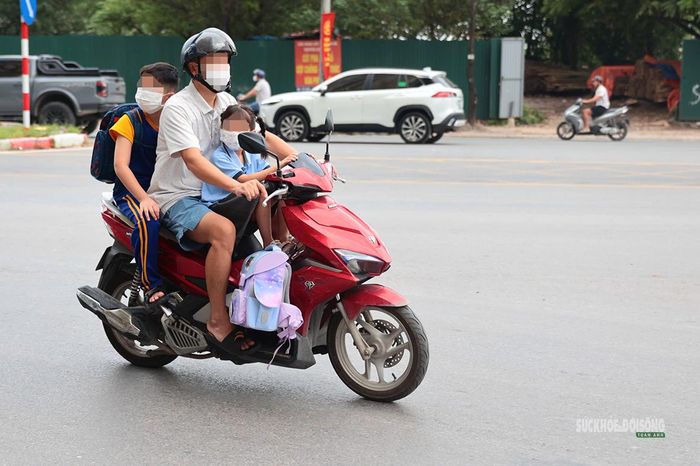 Người đàn ông chở hai trẻ trên xe máy lưu thông qua nút giao. Ảnh: T.Anh