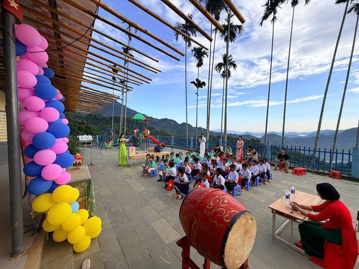 Không khí buổi lễ cũng mang nét hồn nhiên rất riêng của trẻ nhỏ. Một học sinh vẫn còn ngái ngủ khi chương trình đang diễn ra; những em khác cầm cờ Tổ quốc, nở nụ cười trước ống kính. Phía sau khu vực học sinh, nhiều phụ huynh đứng theo dõi buổi lễ. Có người đưa cả con nhỏ đến trường cùng các anh chị