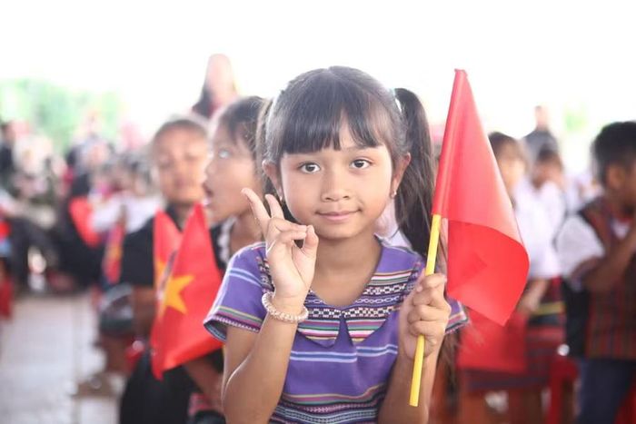 Một nữ sinh người dân tộc thiểu số cầm cờ đỏ sao vàng vui tươi trong ngày tựu trường.