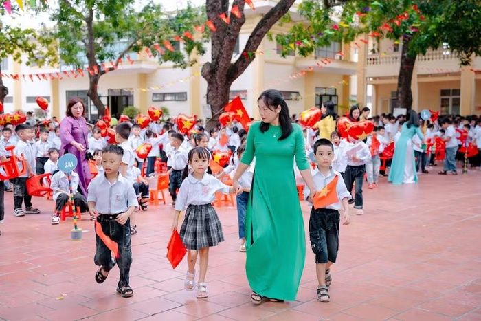 Học sinh lớp 1 tay cầm cờ, nối bước vào sân trường trong sự chào đón của thầy cô và các anh chị lớp trên.