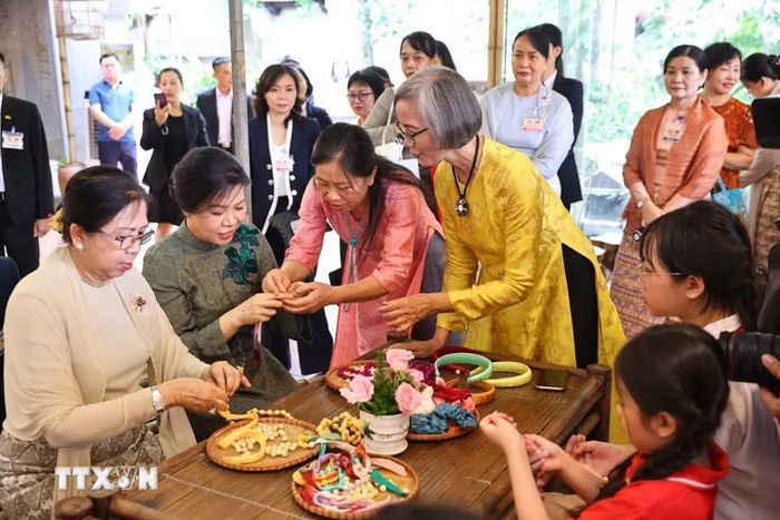 Phu nhân Ngô Phương Ly và Phu nhân Kyu Kyu Hla trải nghiệm xâu vòng lụa với các cháu thiếu niên, nhi đồng của làng nghề. (Ảnh: Minh Đức/TTXVN)