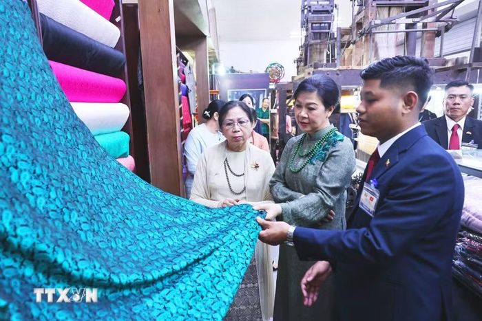 Phu nhân Ngô Phương Ly và Phu nhân Kyu Kyu Hla tham quan khu trưng bày sản phẩm lụa truyền thống và giới thiệu các sản phẩm đặc sắc của làng nghề. (Ảnh: Minh Đức/TTXVN)