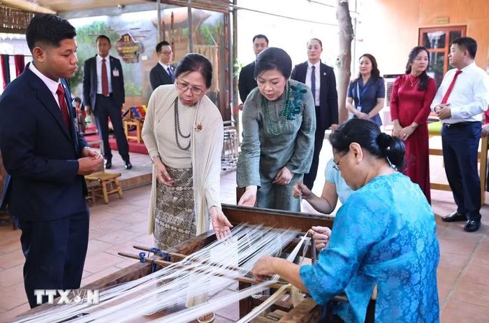 Phu nhân Ngô Phương Ly và Phu nhân Kyu Kyu Hla quan sát khung dệt và xem các nghệ nhân trình diễn dệt lụa. (Ảnh: Minh Đức/TTXVN)