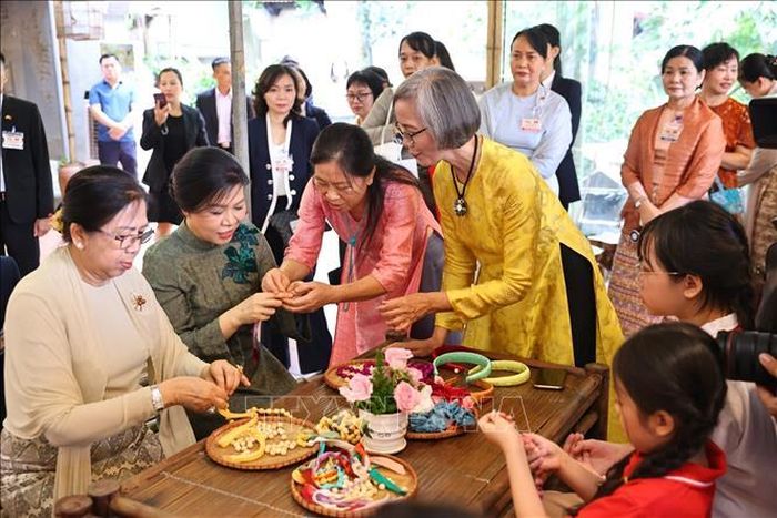 Phu nhân Ngô Phương Ly và Phu nhân Kyu Kyu Hla trải nghiệm xâu vòng lụa với các cháu thiếu niên, nhi đồng của làng nghề. Ảnh: Minh Đức/TTXVN.