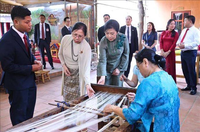 Phu nhân Ngô Phương Ly và Phu nhân Kyu Kyu Hla quan sát khung dệt và xem các nghệ nhân trình diễn nghề dệt lụa. Ảnh: Minh Đức/TTXVN