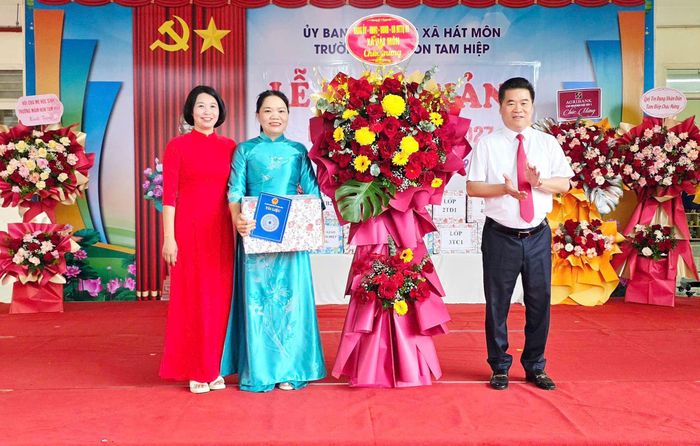 Chủ tịch UBND xã Hát Môn Lý Hoàng Kiên tặng hoa và quà Trường mầm non Tam Hiệp. Ảnh: HM