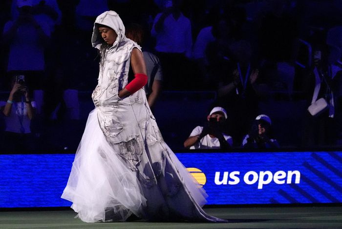  Trên sân, Carlos Alcaraz gây chú ý với áo tank top rộng rãi, phần nách khoét sâu tạo cảm giác phóng khoáng. Naomi Osaka, như thường lệ, xuất hiện với loạt trang phục cầu kỳ, bao gồm áo choàng có mũ in các mẩu báo, kết hợp chân váy tulle trắng; chân váy đen bóng với lớp vải đục lỗ bên dưới; cùng váy Dolce & Gabbana và giày cao gót Sophia Webster khi cô khám phá sân vận động trước thềm giải đấu. Ảnh: Robert Deutsch/Reuters. 