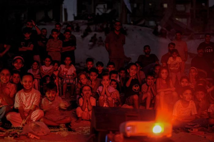  Trẻ em Palestine theo dõi một buổi chiếu phim do sáng kiến Little Wings Cinema tổ chức tại Dải Gaza, trong bối cảnh cuộc sống của người dân nơi đây vẫn chịu nhiều tác động từ tình hình xung đột kéo dài. Dù những hoạt động dành cho trẻ em vẫn được tổ chức để duy trì đời sống cộng đồng, tương lai của người dân Gaza tiếp tục đứng trước một tương lai bất định. (Nguồn: Al Jazeera) 