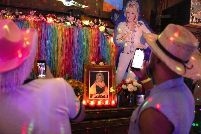  Người hâm mộ chụp ảnh trước một chương trình biểu diễn hóa trang (drag show) tưởng niệm danh ca Dolly Parton tại quán bar Mary’s ở Atlanta, Mỹ, trong những hoạt động tri ân nghệ sĩ này sau khi bà qua đời ở tuổi 80. Sự ra đi của ngôi sao nhạc đồng quê Mỹ ngày 25/8 đã để lại niềm tiếc thương sâu sắc trong giới âm nhạc và đông đảo công chúng Mỹ. Nhiều chương trình truyền hình đặc biệt được phát sóng để tưởng nhớ danh ca, trong khi các nghệ sĩ nhạc đồng quê quy tụ tại Grand Ole Opry ở Nashville để tôn vinh di sản của bà. Nghệ sĩ Dolly Parton được xem là một trong những biểu tượng lớn của âm nhạc Mỹ với sự nghiệp kéo dài gần 70 năm và hơn 3.000 ca khúc, trong đó có những bản nhạc nổi tiếng như Jolene và I Will Always Love You. Bên cạnh âm nhạc, những hoạt động thiện nguyện của bà, đặc biệt là chương trình Imagination Library hỗ trợ sách cho trẻ em, cũng góp phần tạo nên di sản được nhiều thế hệ trân trọng. (Nguồn: The New York Times) 
