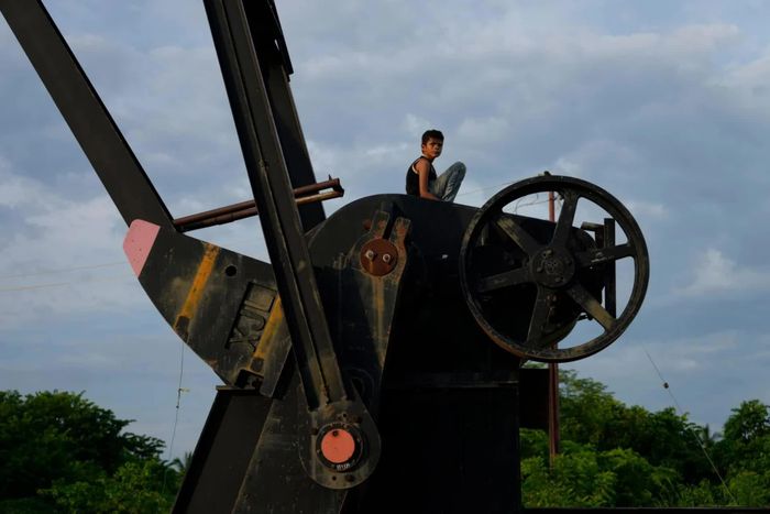  Cậu bé ngồi trên một giàn bơm dầu đã ngừng hoạt động tại Cabimas, Venezuela, ngày 31/8. Hình ảnh tương phản với những kỳ vọng mới về dòng vốn và công nghệ đang được mở ra cho ngành dầu khí Venezuela sau loạt thỏa thuận về lĩnh vực năng lượng. Ngày 2/9, các tập đoàn năng lượng Mỹ và quốc tế ký loạt thỏa thuận đầu tư trị giá hàng chục tỷ USD với Venezuela, chỉ vài ngày sau khi Washington đạt thỏa thuận tiếp cận khoảng 65 tỷ thùng dầu của quốc gia Nam Mỹ này. Trong đó, Chevron dự kiến đầu tư hơn 7 tỷ USD trong 5 năm tới, hướng tới nâng sản lượng tại Vành đai Orinoco lên khoảng 600.000 thùng/ngày. Các thỏa thuận được kỳ vọng tạo thêm động lực cho ngành dầu khí Venezuela sau thời gian dài thiếu đầu tư. Caracas cho rằng, mở rộng hợp tác với Mỹ là cần thiết để thu hút nguồn lực cho lĩnh vực năng lượng. Tổng thống lâm thời Venezuela Delcy Rodriguez ước tính các thỏa thuận có thể mang lại khoảng 209 tỷ USD cho nước này trong 25 năm, qua đó tạo thêm việc làm, tăng thu nhập và cải thiện dịch vụ công. (Nguồn: CNN) 
