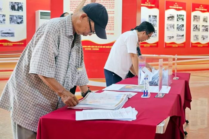 Một công dân cao tuổi nán lại bên bàn hồ sơ, cẩn thận đối chiếu từng trang tài liệu kỹ thuật để nắm rõ phương án bảo tồn và cải tạo không gian quanh hồ.