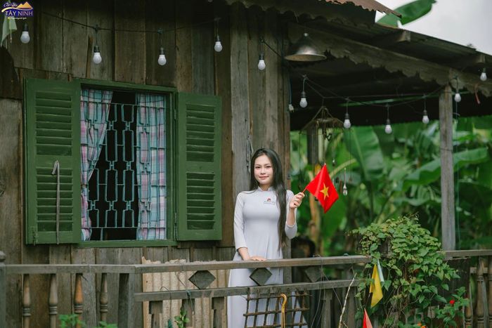  "Nhà ông nội" mang dáng vẻ của một căn nhà miền quê với sàn thấp, vách gỗ, mái lợp tôn. Cánh cửa sổ gỗ được sơn màu xanh lá trùng với màu áo lính. Để phù hợp với nội dung truyền tải của bộ phim về thời kháng chiến, nhiều bạn trẻ lựa chọn trang phục kín đáo hoặc áo dài trắng khi đến chụp ảnh. Ảnh: Trí Dương. 