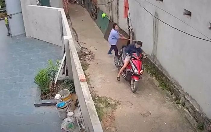 Người phụ nữ áo xanh cầm chổi đánh mạnh vào đầu hàng xóm. Ảnh: Cắt từ clip
