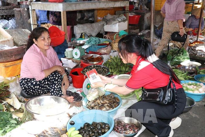 Hướng dẫn tiểu thương sử dụng bảng mã QR. Ảnh: Thanh Hòa- TTXVN