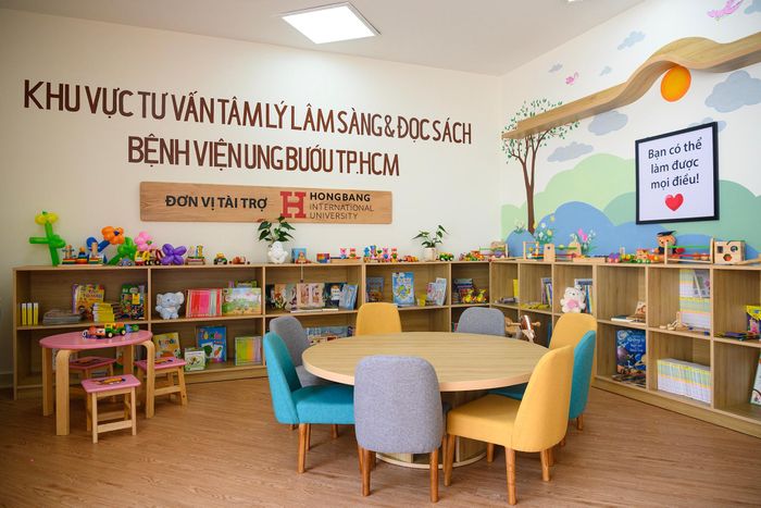  Căn phòng được thiết kế hiện đại, ấm cúng với màu gỗ sáng kết hợp cùng sắc xanh, vàng rực rỡ từ những chiếc ghế nhỏ. Hệ thống kệ sách chạy dọc tường lưu trữ hàng trăm đầu sách thiếu nhi phong phú, được sắp xếp ngăn nắp và vừa tầm với của các em nhỏ. Chiếc bàn tròn lớn ở giữa là không gian sinh hoạt chung thoải mái, nơi các bé có thể cùng nhau đọc sách, vẽ tranh hay trò chuyện. 