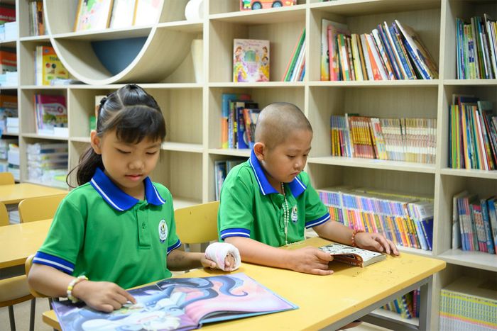  Cô bé An Nhiên (9 tuổi, ngồi bên trái) đã điều trị tại Bệnh viện từ năm 4 tuổi tỏ ra thích thú với cuốn sách mới. Những trang sách có tranh sinh động, truyện cổ tích về nàng tiên cá hay bộ truyện trinh thám Conan luôn có sức hút đặc biệt với em. Mỗi cuốn sách mở ra là một niềm vui nho nhỏ tiếp thêm năng lượng tích cực cho cô học trò lớp 4. 