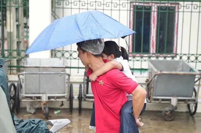 Trời mưa, phụ huynh cõng con đi về nhà sau khi trường tạm dừng tổ chức ăn bán trú.