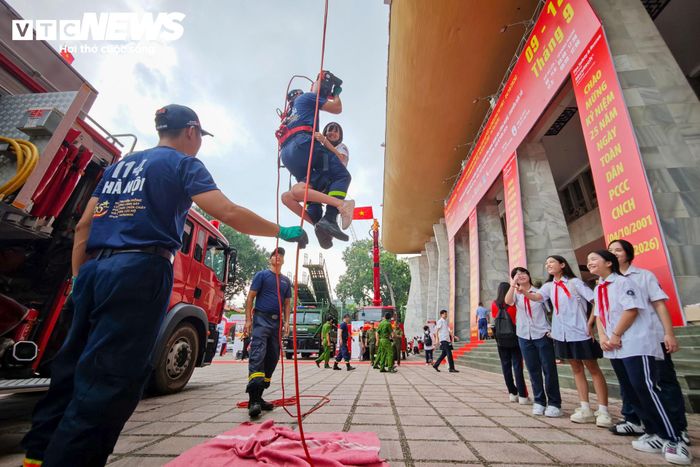 Tại khu vực tháp cứu hộ, các chiến sĩ PCCC thực hiện bài thực hành đưa người được giả định là nạn nhân từ trên cao xuống đất. Một chiến sĩ ôm chặt nạn nhân, sử dụng dây chuyên dụng di chuyển từ đỉnh tháp xuống trong sự theo dõi của đông đảo học sinh và khách tham quan.
