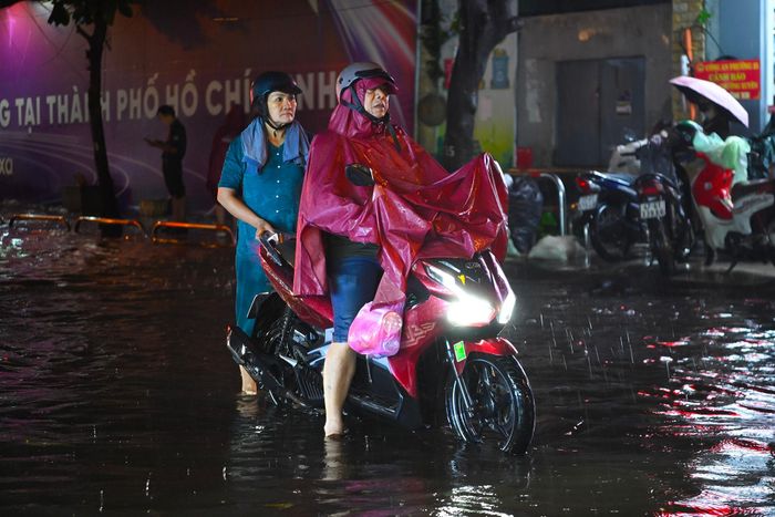 Không thể tiếp tục chạy xe qua vùng nước sâu, một số người chọn cách xuống xe rồi dắt bộ. Người dân vừa phải giữ phương tiện, vừa tìm cách di chuyển giữa dòng xe đông và mặt đường ngập nước. Hành trình về nhà trong giờ cao điểm vì thế kéo dài hơn nhiều so với thường ngày.