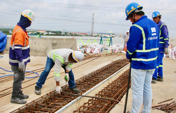 Tại phía bờ TP.HCM, một nhóm công nhân đang khẩn trương hoàn thiện khe co giãn cuối cùng. Cách đó không xa, các tốp thợ khác đồng thời lắp đặt hệ thống chiếu sáng, hoàn thiện mặt cầu, chuẩn bị cho công đoạn thảm bê tông nhựa.