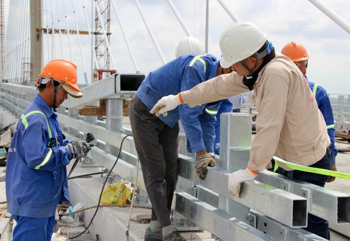 Công nhân Hoàng Văn An (giữa) cho biết, nhìn cây cầu từ chỗ còn dang dở đến nay đã gần hoàn thành anh em công trường rất phấn khởi. “Chỉ mong thời tiết thuận lợi để đẩy nhanh những phần việc cuối cùng để sớm thấy từng dòng xe băng băng qua cầu”, anh An nói.