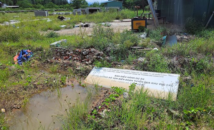Tại khu vực phía Nam cầu Hà Tây, ngoài những cấu kiện bê tông đã đúc, một thiết bị xe máy nằm bất động bên số sắt thép phơi mưa nắng hoen gỉ. Tấm biển nhà thầu phụ Công ty TNHH Xây dựng và Thương mại Song Phú nằm trên vũng nước cạnh nhà của ban điều hành đang đóng cửa.