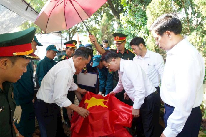 Lãnh đạo phường Chương Mỹ thực hiện nghi thức phủ Quốc kỳ lên hài cốt liệt sĩ trước khi đưa đến khu vực lấy mẫu. Ảnh: Lan Oanh