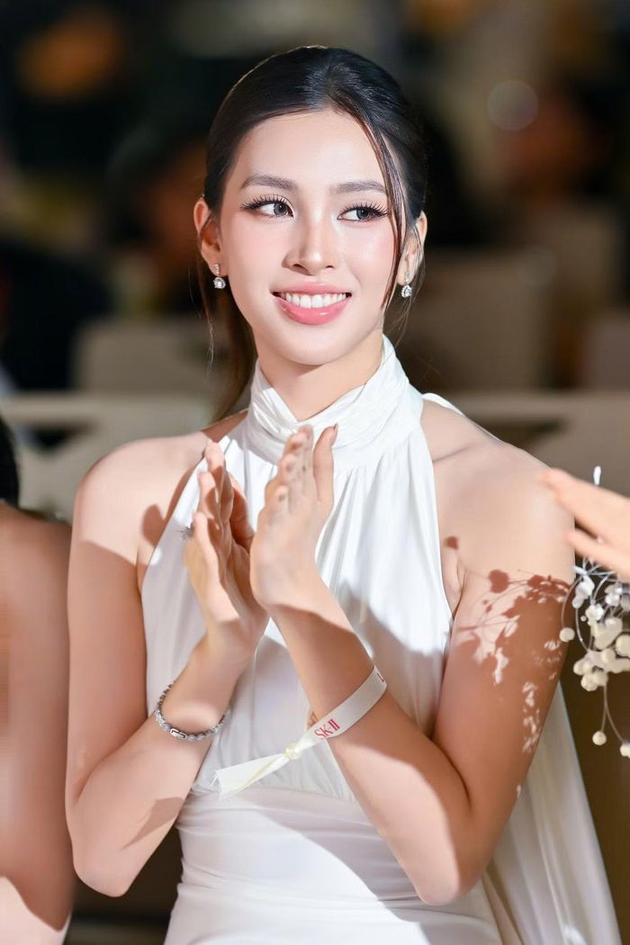 Hoa hậu Tiểu Vy diện đầm trắng cổ yếm, thân váy ôm sát vóc dáng. Kiểu tóc búi gọn để lộ vai, kết hợp khuyên tai đính đá và vòng tay nhỏ. Cô chọn cách trang điểm nhấn vào hàng mi, dùng son hồng nhạt khi tham dự buổi gặp gỡ có nữ diễn viên Thái Lan.