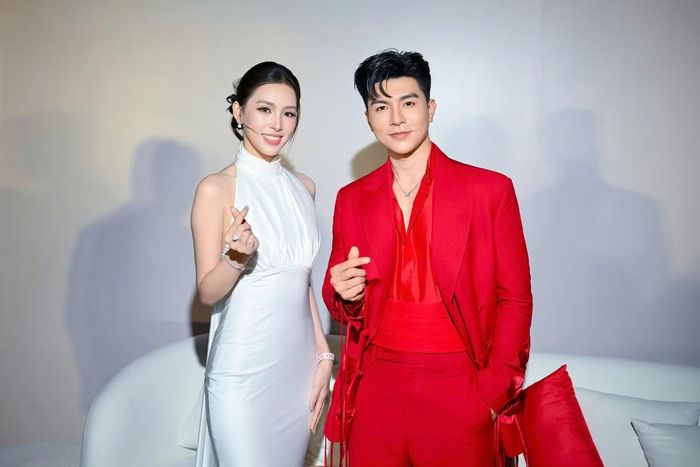 Tiểu Vy chụp ảnh cùng Steven Nguyễn. Nam diễn viên chọn suit đỏ, kết hợp áo cùng màu có chi tiết dây buộc và phần đai xếp nếp ngang eo.